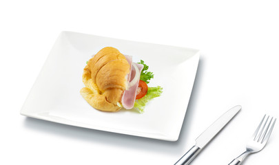 Big croissant with green salad and pork meat on isolate white background. Tasty croissant with a fork and knife place beside the plate. Food photo. Healthy food concept.