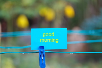 Conceptual photo: Blue clothes peg with blue note written "Good morning". Selective focus