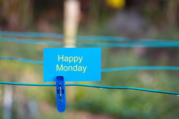 Conceptual photo: Blue clothes peg with blue note written "Happy Monday". Selective focus