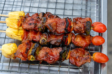 Skewers with pieces of grilled barbecue, green bell pepper, red tomato and meat for sell in street market, Thailand, closeup