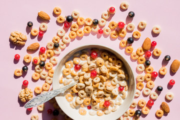 wholegrain flakes with berries and milk on pink. Healthy tasty breakfast cornflakes with blueberries, raspberries and red currant.Multigrain wholewheat healthy cereals with fresh berry.
