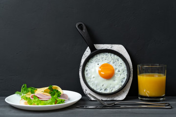Breakfast of fried eggs in pan, toast with cheese, ham, lettuce, and orange juice. Delicious nutritious breakfast.