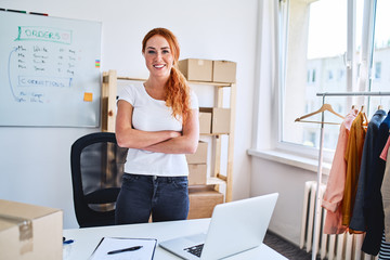 Portrait of young woman smiling at camera with crossed arms while standing in office of her new...