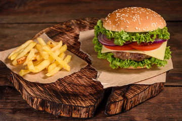 Tasty grilled homemade burgers with beef, tomato, cheese, cucumber and lettuce. Delicious grilled burgers. Craft beef burger and french fries on wooden table
