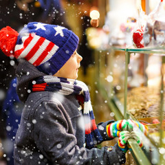 Little cute kid boy near sweet stand with gingerbread and nuts. Happy child on Christmas market in...