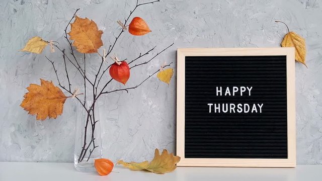 Happy Thursday text on black letter board and bouquet of branches with yellow leaves on clothespins in vase on table Template for postcard, greeting card Concept Hello autumn Thursday.
