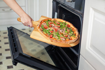 Close-up. Woman hand put pizza in the oven.