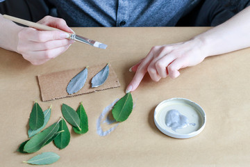 Woman paints on silver color leaves and autumn fruits
