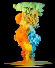 Colorful paint drops from above mixing in water. Ink swirling underwater. Green, orange, blue colors.