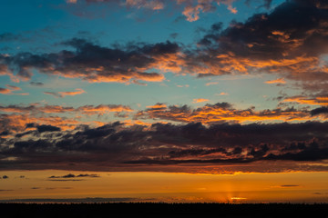 Obraz premium Evening sky at sunset background. Dark clouds hanging above horizon. Majestic cloudscape in blue, orange, violet shades. Grey cloudlets bringing rain. Countryside skyline in twilight time
