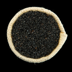 Black sesame in a bag isolated on a black background. View from above. Seasoning on isolate. Dry spices.