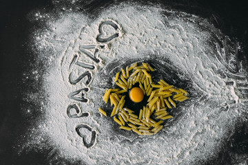 raw broken chicken egg on the table, pasta lies around it. Flour is scattered on the table the inscription pasta on it