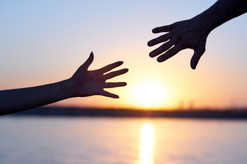 Giving a helping hand. Silhouette Two hands, man and woman, reaching towards each other at sky sunset