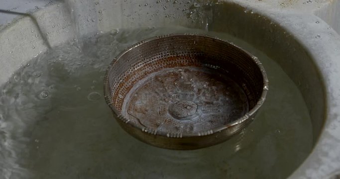 Close-up of slow motion water flows from the tap into the storage tank and an old Cup for watering the body in the Turkish bath Hammam