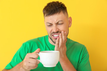 Man with sensitive teeth and hot coffee on color background