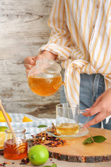 Woman pouring tasty hot beverage from teapot into cup at table