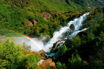 Green mountain forest through waterfall rainbow on the way to Briksdal