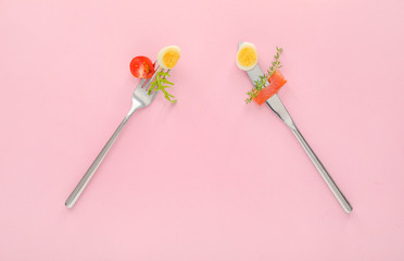 Forks with quail eggs, salmon, tomato and herbs on color background