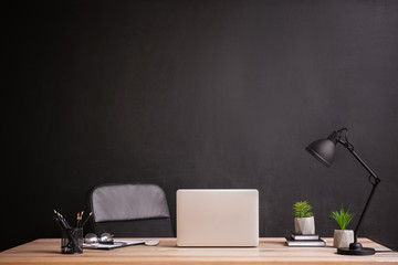 Stylish workplace with modern laptop near dark wall