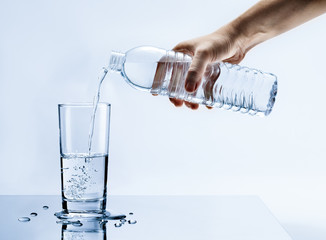 Hand pouring fresh pure water from bottle into a glass on the table with water drops, Healthcare and beauty hydration concept