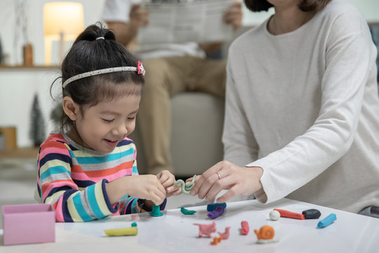 Mom with her daughter playing with a colorful toys modeling clay on the floor, at background daddy is sitting in a sofa in the living room, Happy asian family at home - Powered by Adobe