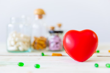 Healthcare and medical concept. Red heart on wooden table with set of medicine bottles and medicine pills background. Copy space for your text.