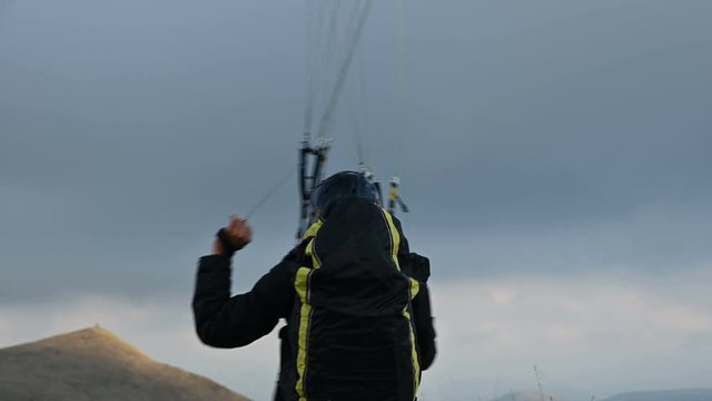 A male athlete paraglider raises a wing in an outdor against the backdrop of evening clouds but cannot fly. Failure while trying to take off