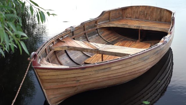 A wooden boat without oars is tied at the pier with a tree and sways in the waves