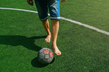 European football, lack of money for sports shoes and a new ball. Football player without shoes and an old ball, on a green new artificial field.   
