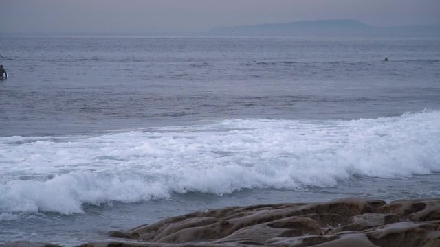 Wave near the ocean coast with surfers on background. Slow motion