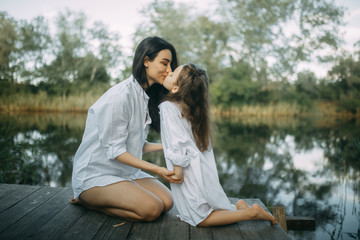 Mother and daughter kiss and have fun near a small river.