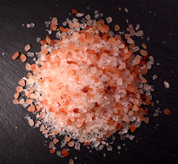 Pile of pink Himalayan salt. Top view on a dark stone background.