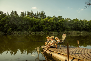 Cute little girls and their granddad are on fishing at the lake or river. Resting on pier near by...