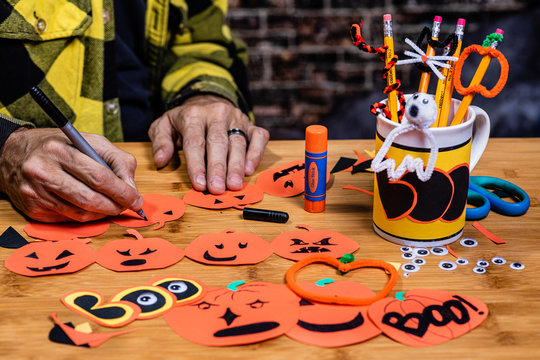 An adult male making making construction paper jack-o-lanterns, focus is on the Marker Tip.  Many crafts are on the table with tools.