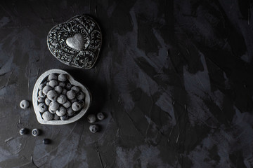 Blueberries with hoarfrost in a silver box heart on a dark background