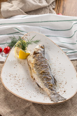 Grilled whole trout fish with lemon on white plate on tablecloth