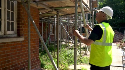 Male builder foreman construction worker on building site inspecting and checking scaffolding for health and safety