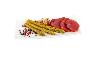 A small plate with asparagus, herbs and cured sausage on a white background.