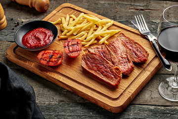 Medium rare sirloin steak with chips and red wine on a rustic wooden table with ethnic tablecloth. Classic European lunch.