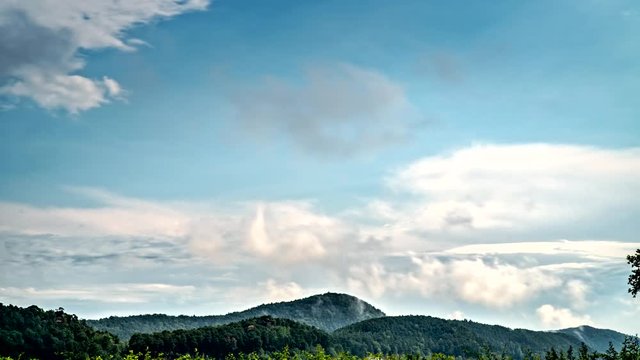 Timelapse of different layers of clouds moving fast and slowly above european wooded hills 4K