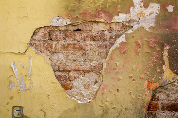 heavily damaged concrete wall with cracks, peeling paint and old red brickwork. rough surface texture