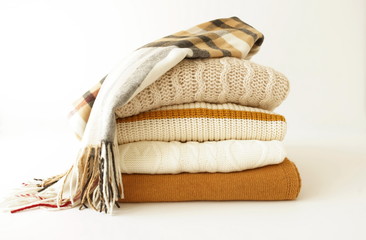Stack of sweaters and scarf in pastel colors on white background. Copy space