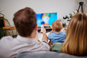 Young parents watching TV with baby boy.