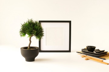 Black frame mock up poster, bonsai tree and sushi set on the white desk. Home decor close up. Copy space
