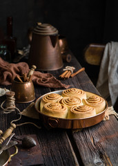 Homemade cinnamon roll buns in vintage copper round pan on wooden rustic table 