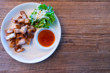 Fried pork belly on a white plate with salad.