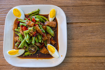 Som Tum mixed with Lentils,crispy pork, pickled fish on a white plate and old wooden table.