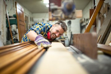 Portrait of experienced carpenter worker cutting wood plank on the machine in his woodworking workshop.