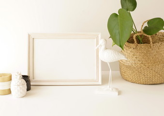 White frame mock up on white wall, home plant monstera in straw basket flowerpot, white bird figure...