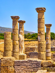 Remains of the main Basilica and the statue of the Roman Emperor Trajan in Baelo Claudia Archaeological Site. Tarifa, Cadiz. Andalusia, Spain.